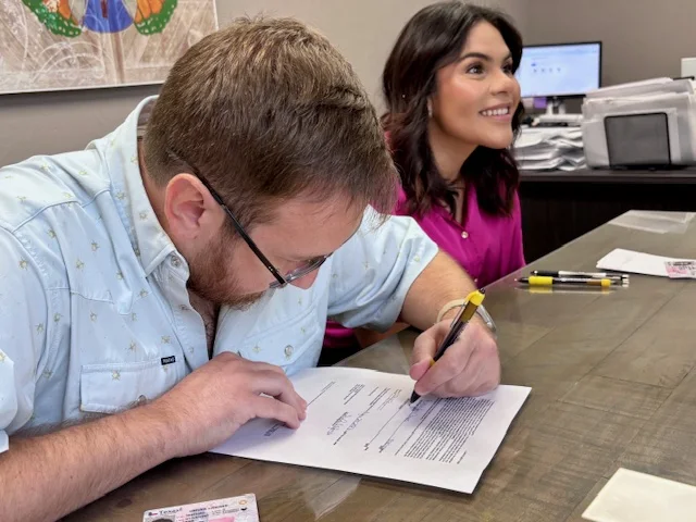 A home buyer signing closing paperwork with Hilary Wesley nearby